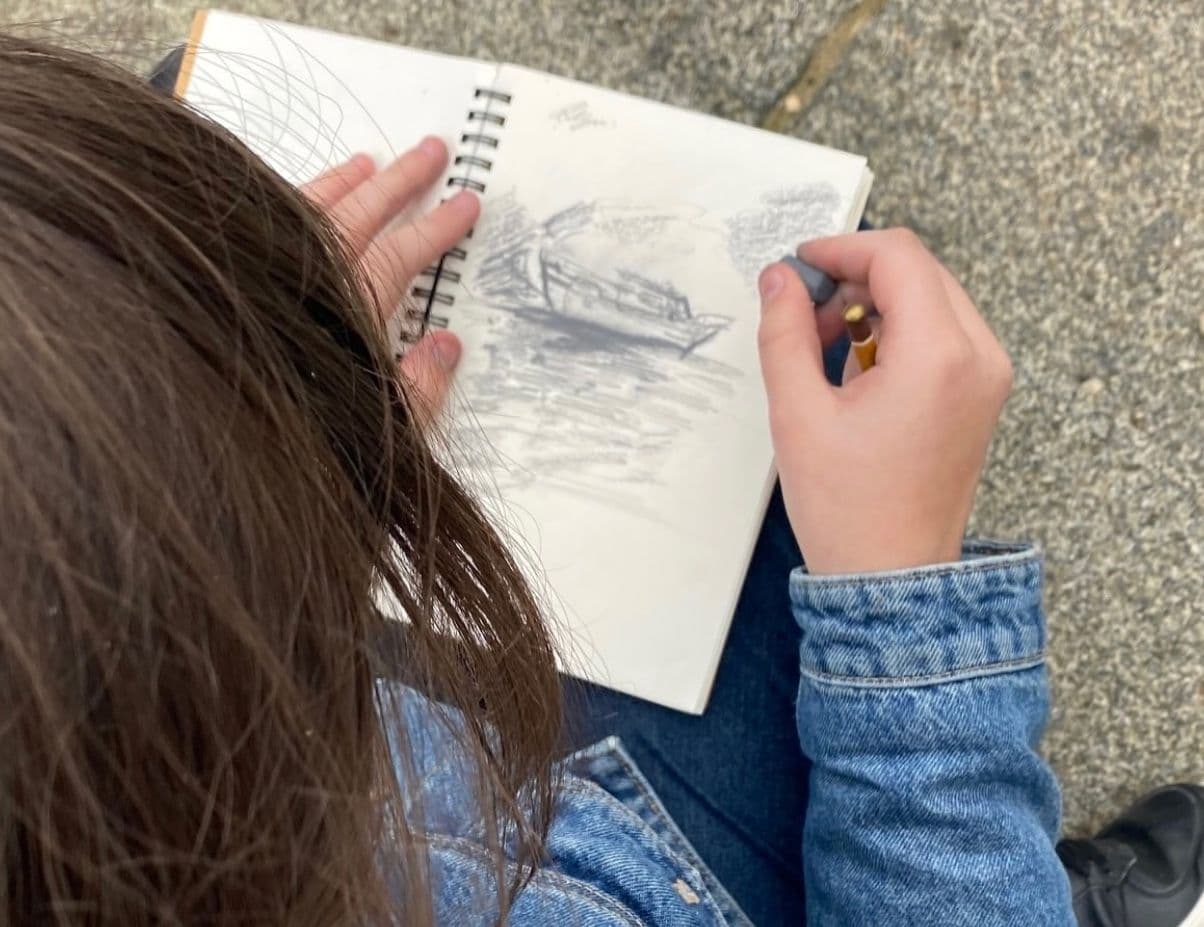 Kind zeichnet mit Kohle auf einem Heft ein Schiff